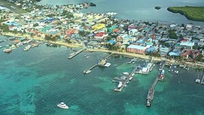 Vista aérea de uma cidade costeira com um porto de iates, edifícios coloridos e águas turquesa cristalinas.