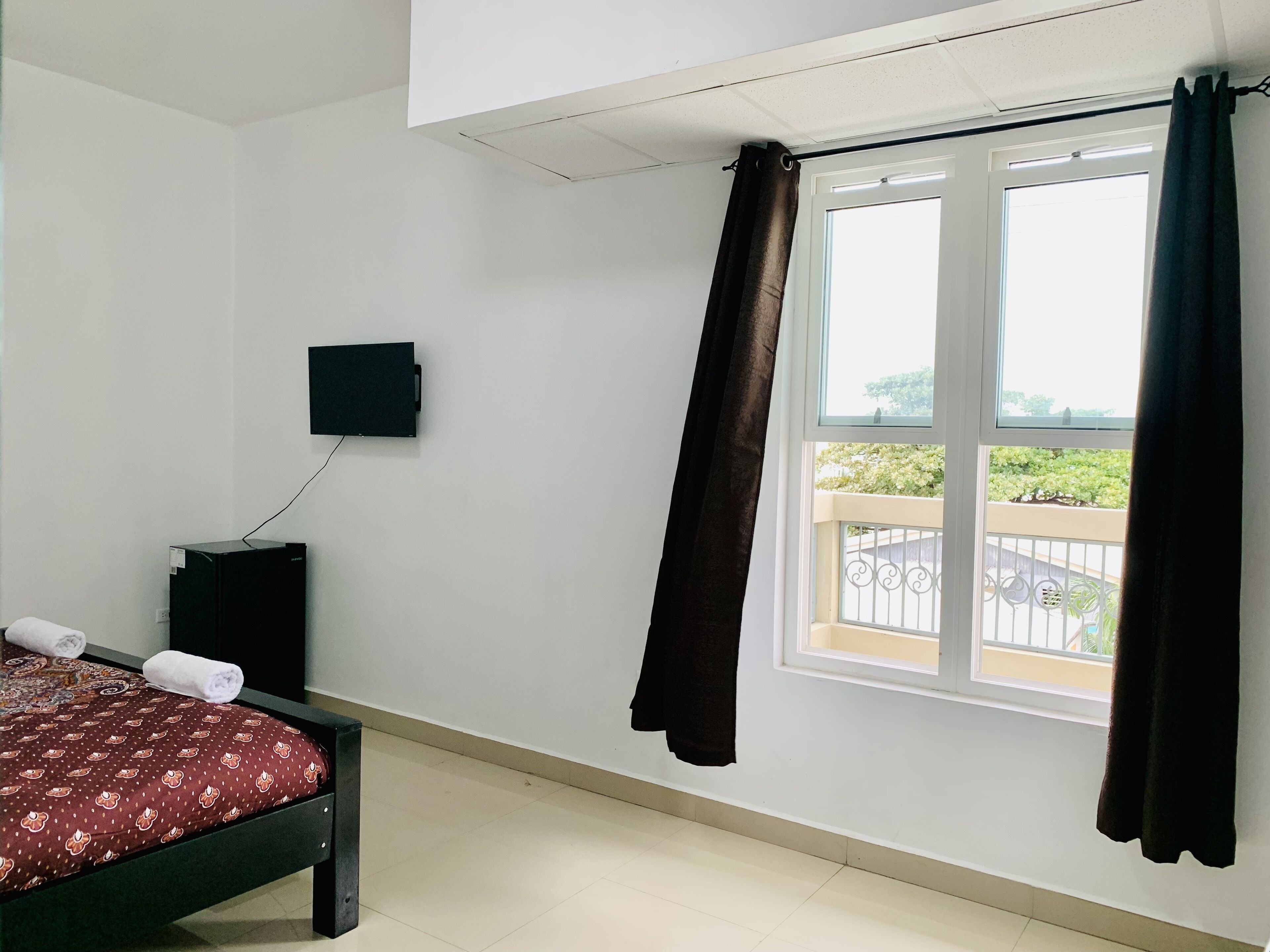 Un dormitorio con una cama, un televisor montado en la pared y una ventana con cortinas.