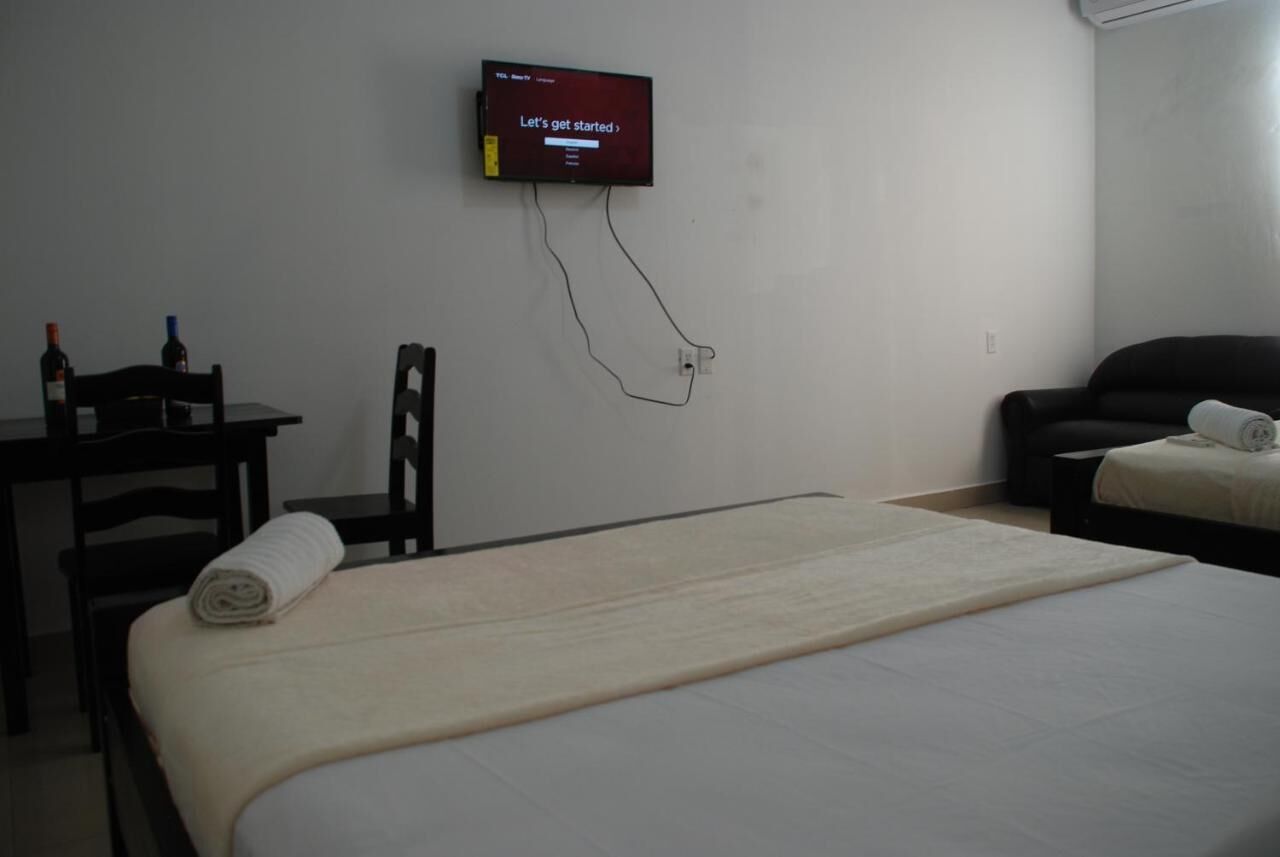 Habitación de hotel con una cama, un escritorio, una silla, un televisor montado en la pared y una mesita con dos botellas.