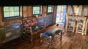 A rustic wooden room with a bench and chairs, a small table, and a window with a view of greenery. - Rustic Cabin on 7 Acres (Sparta)