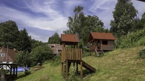 Een houten constructie in rustieke stijl met een trap die leidt naar een platform, omgeven door weelderige begroeiing en een heldere lucht.