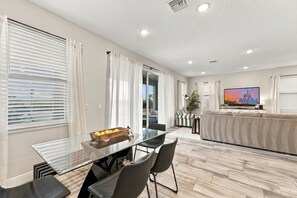 Un salon moderne avec une table à manger en verre, des chaises noires, un canapé et un téléviseur.