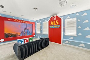 A room with a large flat-screen TV, a red wall with a toy barn sign, and a blue wall with cloud decals.
