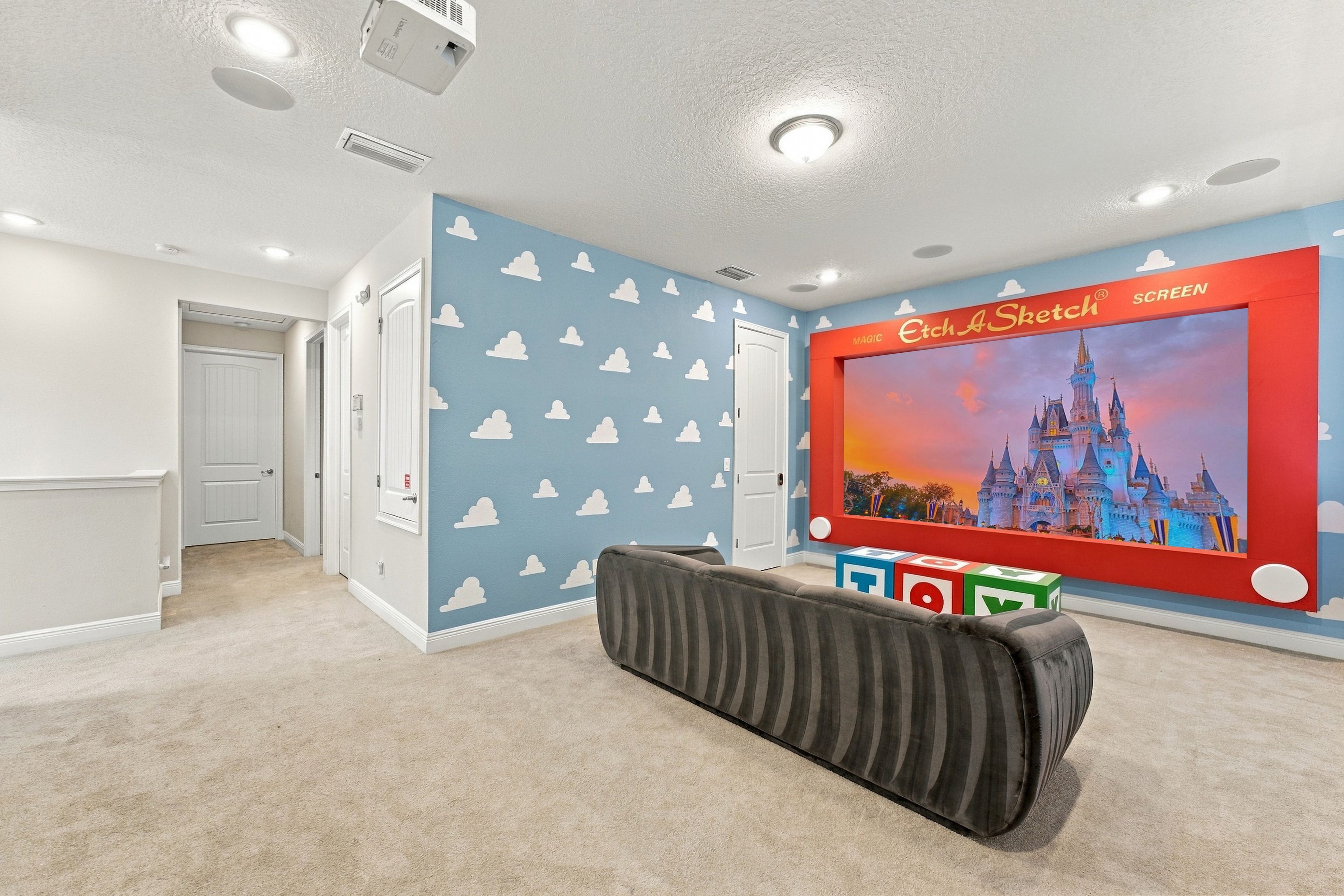 A room with a large screen displaying a castle, a projector, and a play area with colorful blocks.