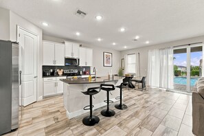 A modern kitchen with white cabinets, a central island, and bar stools. - Magical Memories Villa: Pop Culture, Pool, Near Disney (Kissimmee)