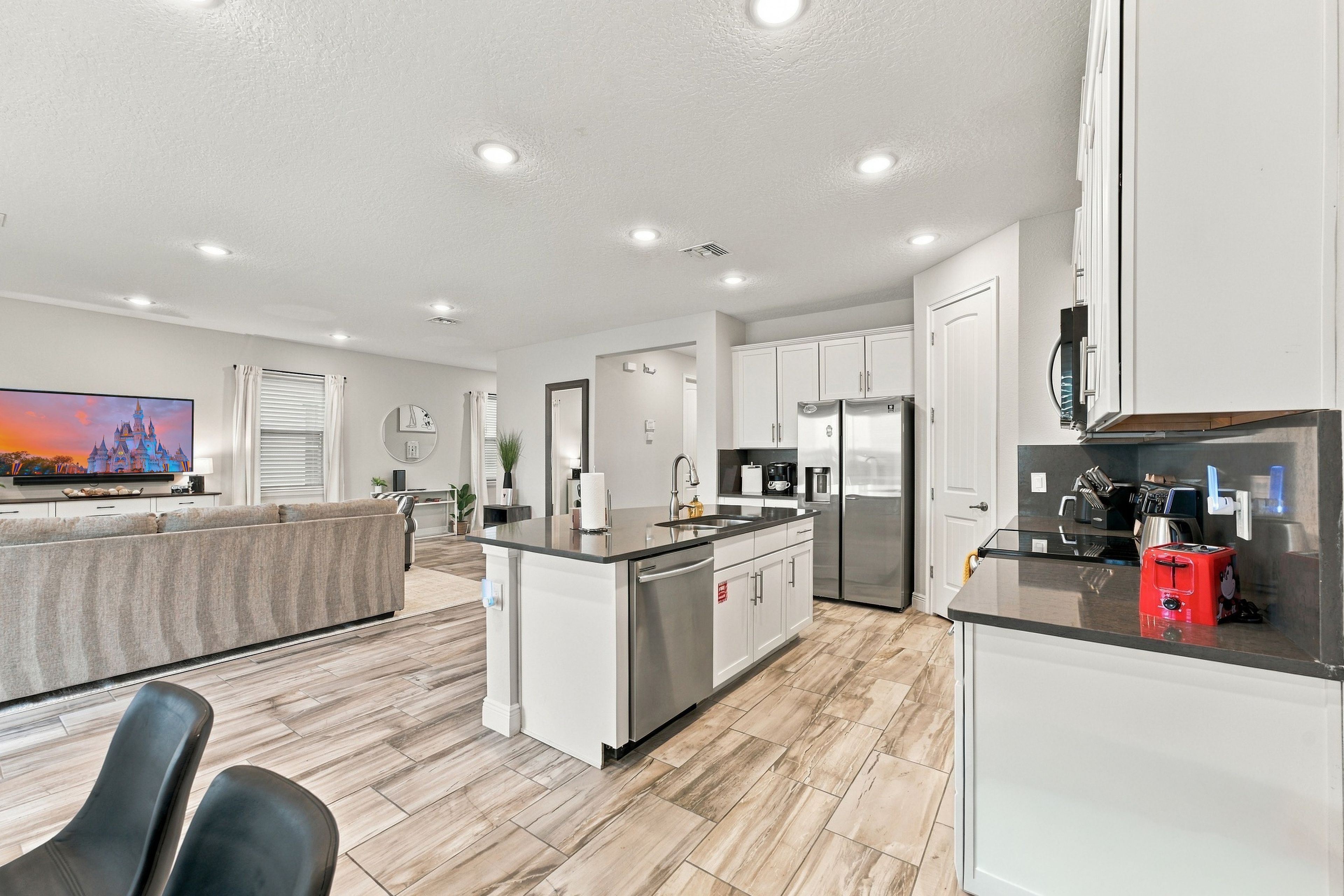 A modern kitchen with a central island, stainless steel appliances, and a flat-screen TV mounted on the wall.