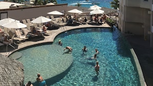 Zona de piscina con sillas de descanso y sombrillas, vista despejada del océano y un crucero a lo lejos.