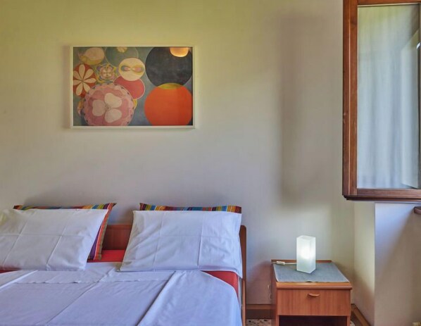 A bedroom with two beds, a nightstand with a lamp, and a painting on the wall.