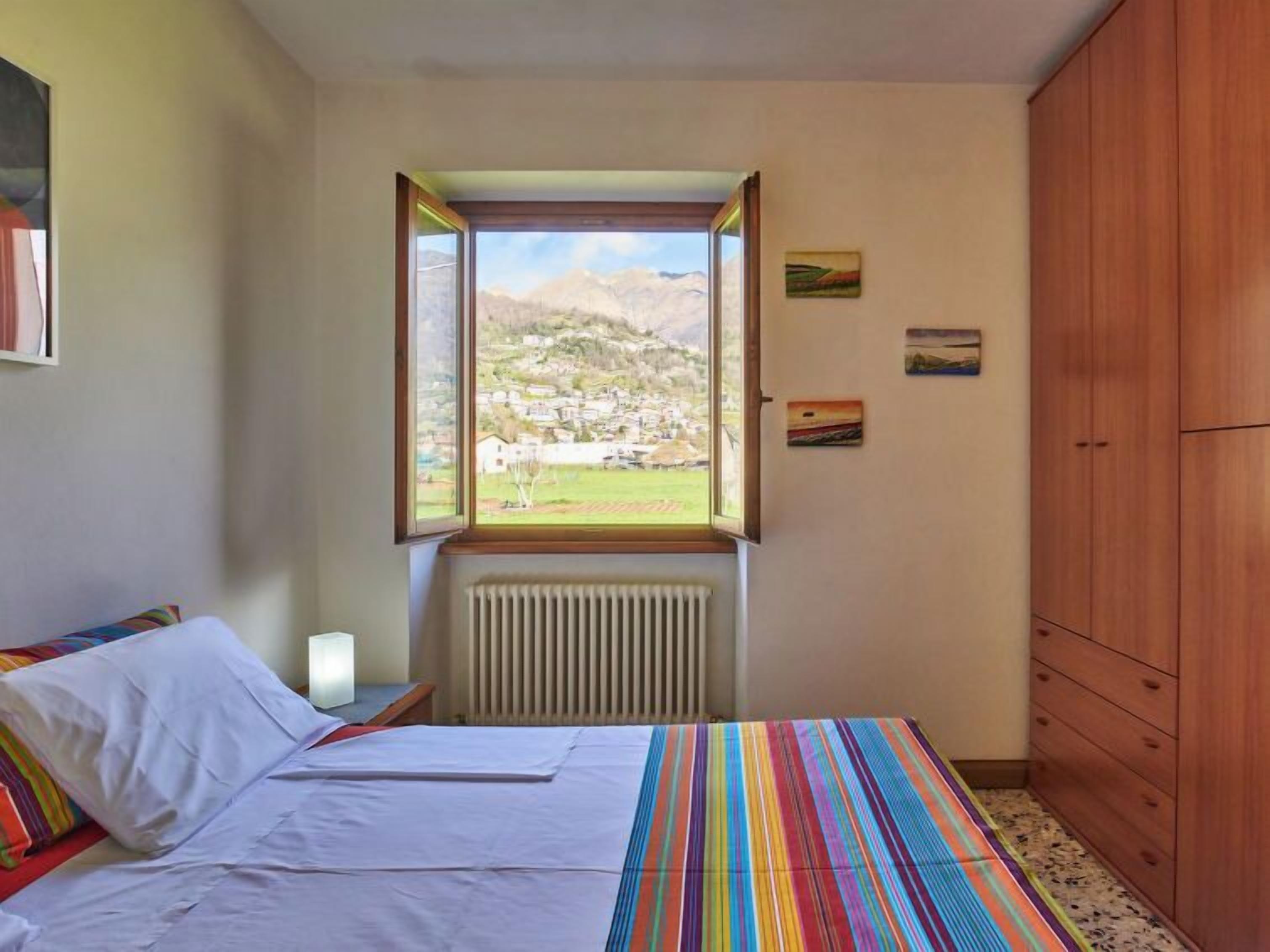 Un dormitorio con cama, ventana con vistas a un pueblo, radiador y muebles de madera.