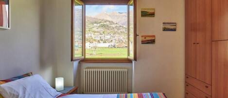 Un dormitorio con cama, ventana con vistas a un pueblo, radiador y muebles de madera.