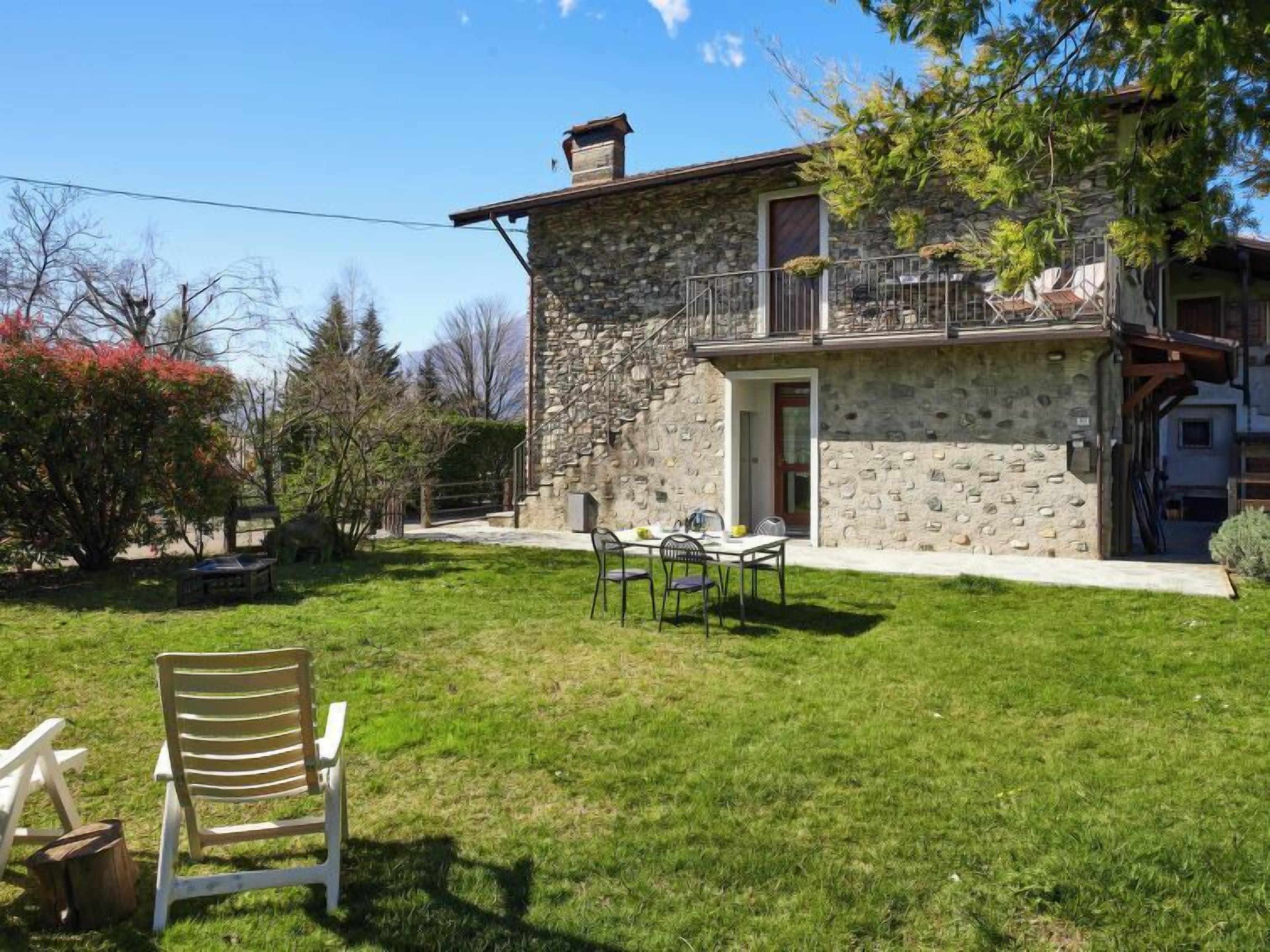 A stone house with a balcony, a grassy yard, and outdoor furniture.