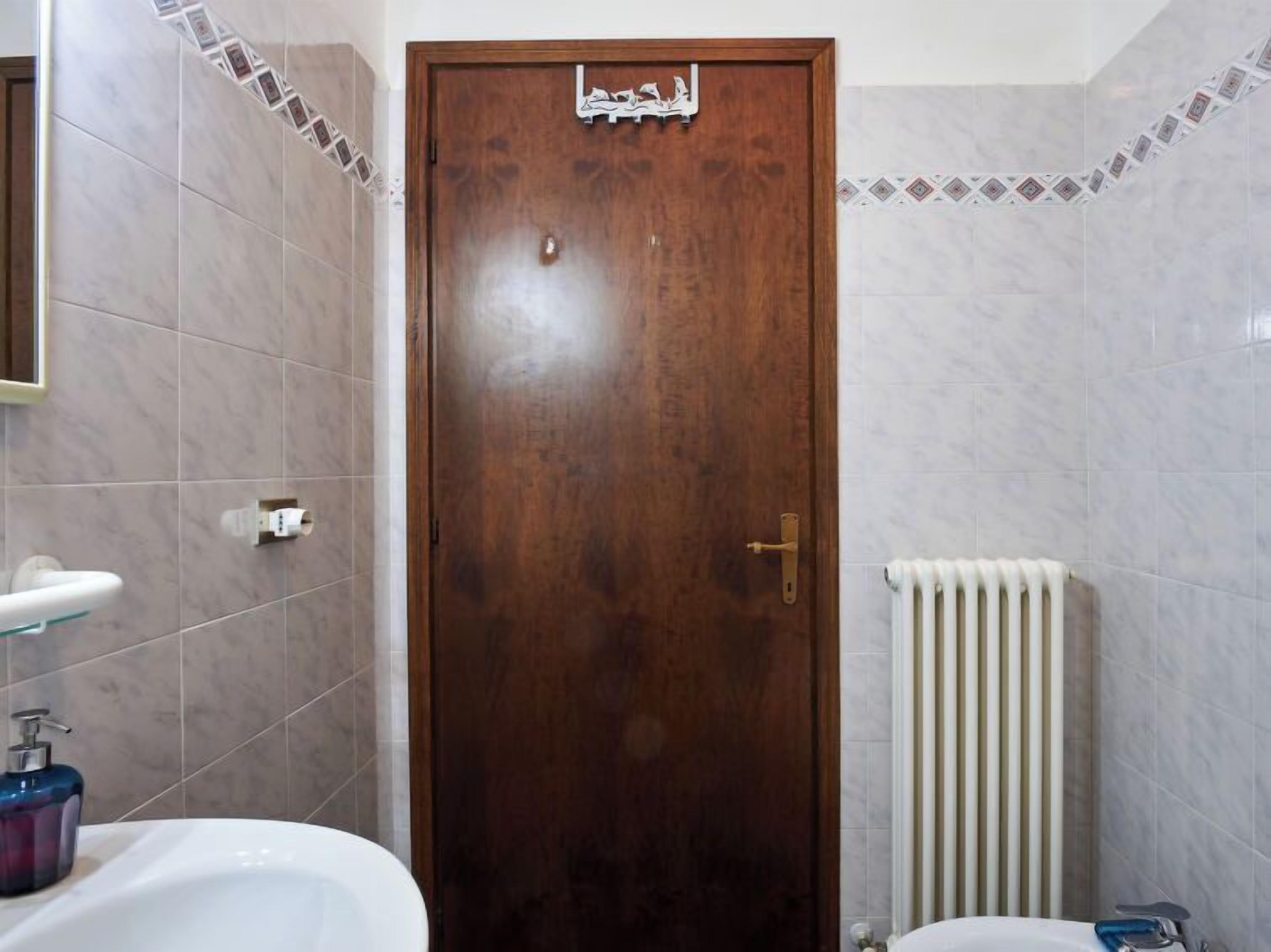 Ein Badezimmer mit Holztür, Waschbecken, Toilette und Heizkörper.