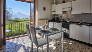 Eine moderne Küche mit weißen Schränken, ein Essbereich mit Tisch und Stühlen sowie Blick auf einen See und Berge durch ein großes Fenster.