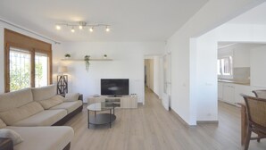A modern living room with a sofa, TV, and a small table. There is a kitchen area visible through an open door. - To rent house with private pool in Begur, center (Begur)