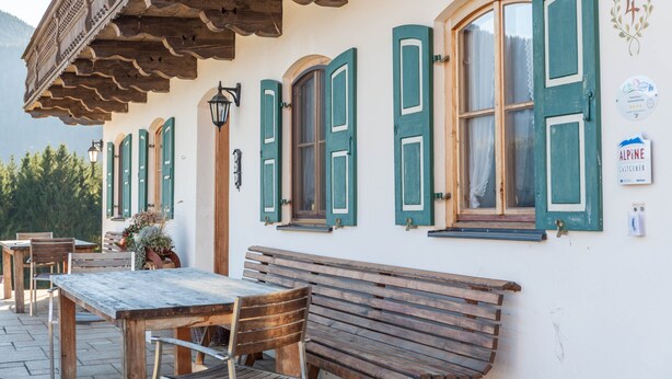 Een traditioneel gebouw met houten banken en tafels, een balkon met houten leuning en uitzicht op de bergen.