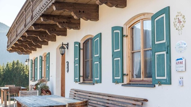 A traditional building with wooden benches and tables, green shutters, and a sign indicating it's an alpine location. - Holiday Apartment Guffertblick with Mountain View, Wi-Fi (Jachenau)
