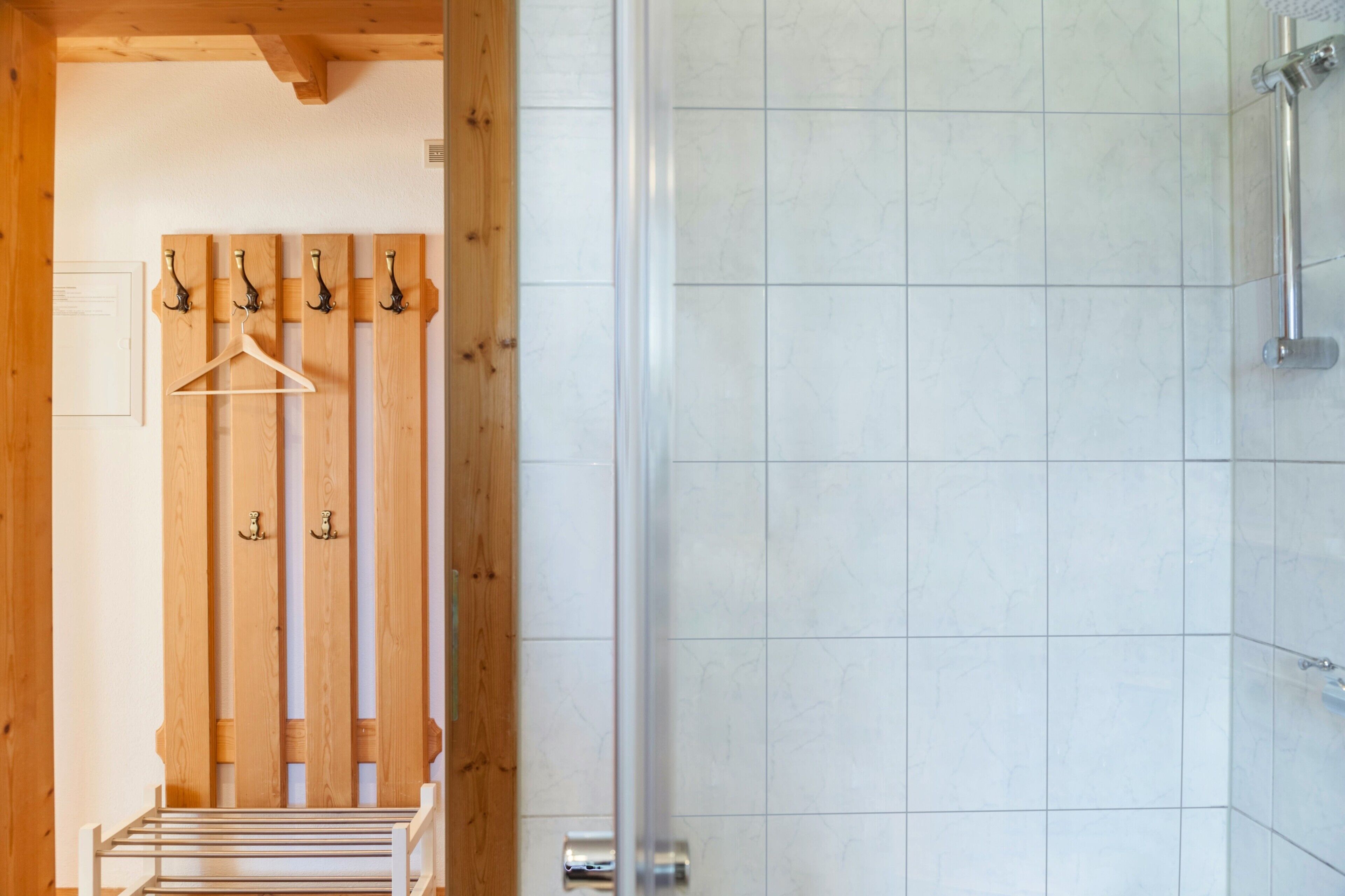 Un espace douche doté d’une porte en verre, un porte-manteau en bois avec des cintres et un porte-serviettes.