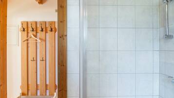 Un espace douche doté d’une porte en verre, un porte-manteau en bois avec des cintres et un porte-serviettes.