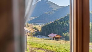 A view through a window of a rural landscape with a mountain, a small building, and a fenced area. - Holiday Apartment Guffertblick with Mountain View, Wi-Fi (Jachenau)