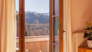 A room with a view of a forest and mountains through an open window. - Holiday Apartment Guffertblick with Mountain View, Wi-Fi (Jachenau)