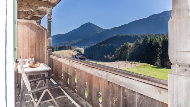 Ein Holzbalkon mit Tisch und Stühlen mit Blick auf eine gebirgige Landschaft.