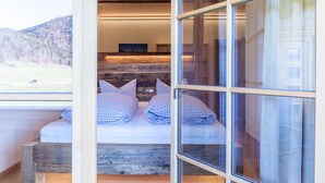 Ein Zimmer mit einem Bett, einem hölzernen Kopfteil und Blick auf eine Berglandschaft durch große Fenster.