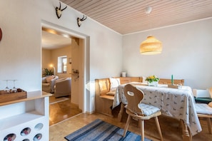 Una habitación acogedora con techo de madera, una mesa de comedor con mantel estampado, una araña y un banco de madera.