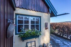 Un edificio rústico con una ventana, una maceta colgante y un muro de piedra.