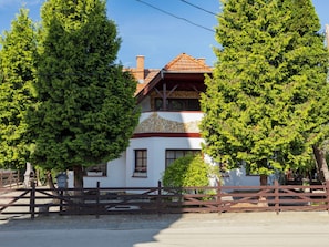 A two-story house with a stone facade, wooden roof, and a wooden fence in front.