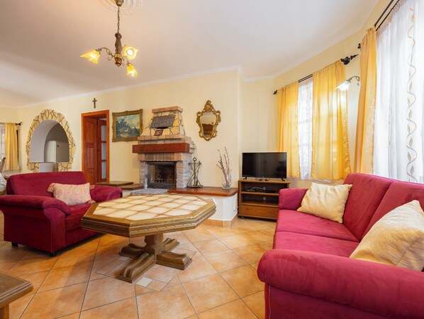 A living room with red sofas, a fireplace, a television, and a chandelier.