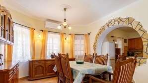 A dining area with a table set for four, surrounded by wooden chairs. There is a chandelier above the table, and the room has a stone archway leading to a kitchen area. - Vacation home Tamas by Interhome (Balatonoszod)