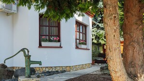 A white building with stone accents, a stone well, and a tree in the foreground. - Vacation home Tamas by Interhome (Balatonoszod)