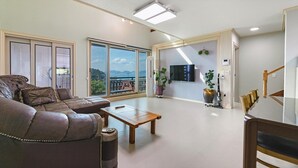 A spacious living room with a leather sofa, a wooden coffee table, and a large sliding glass door leading to a balcony with a view of the sea.
