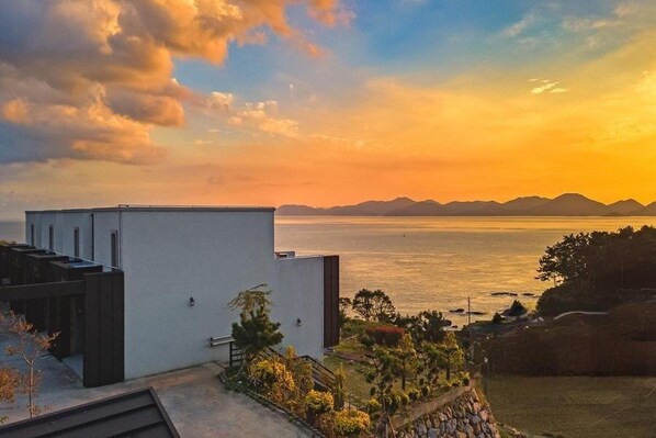 A modern building with a flat roof and a view of the ocean at sunset.