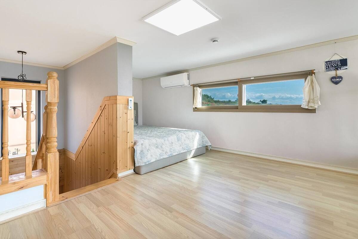 Een slaapkamer met een bed, een raam met uitzicht, een houten trap en een airconditioning.