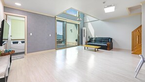 A spacious living area with a wooden floor, a black leather sofa, a wooden coffee table, and a sliding glass door leading to a balcony.