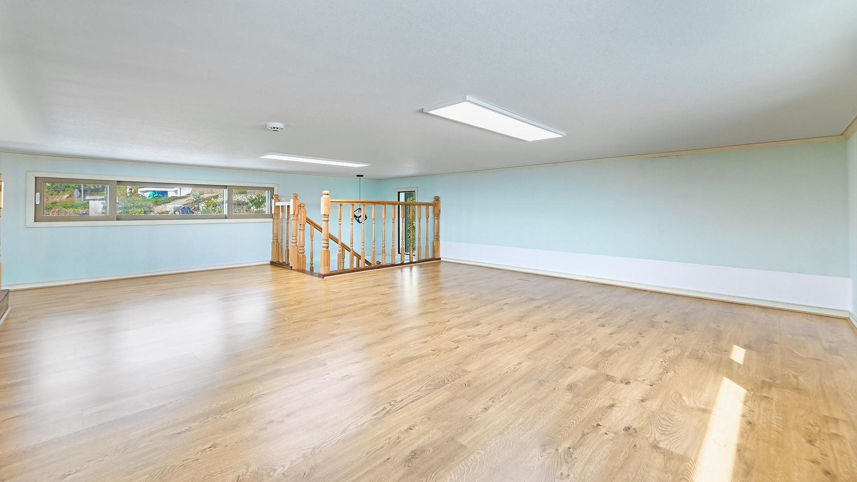 Amplia habitación con piso de madera, una escalera y un ventanal que ofrece vistas al exterior.