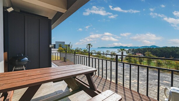 A balcony with a wooden table and chairs, overlooking a scenic view of a body of water and mountains.