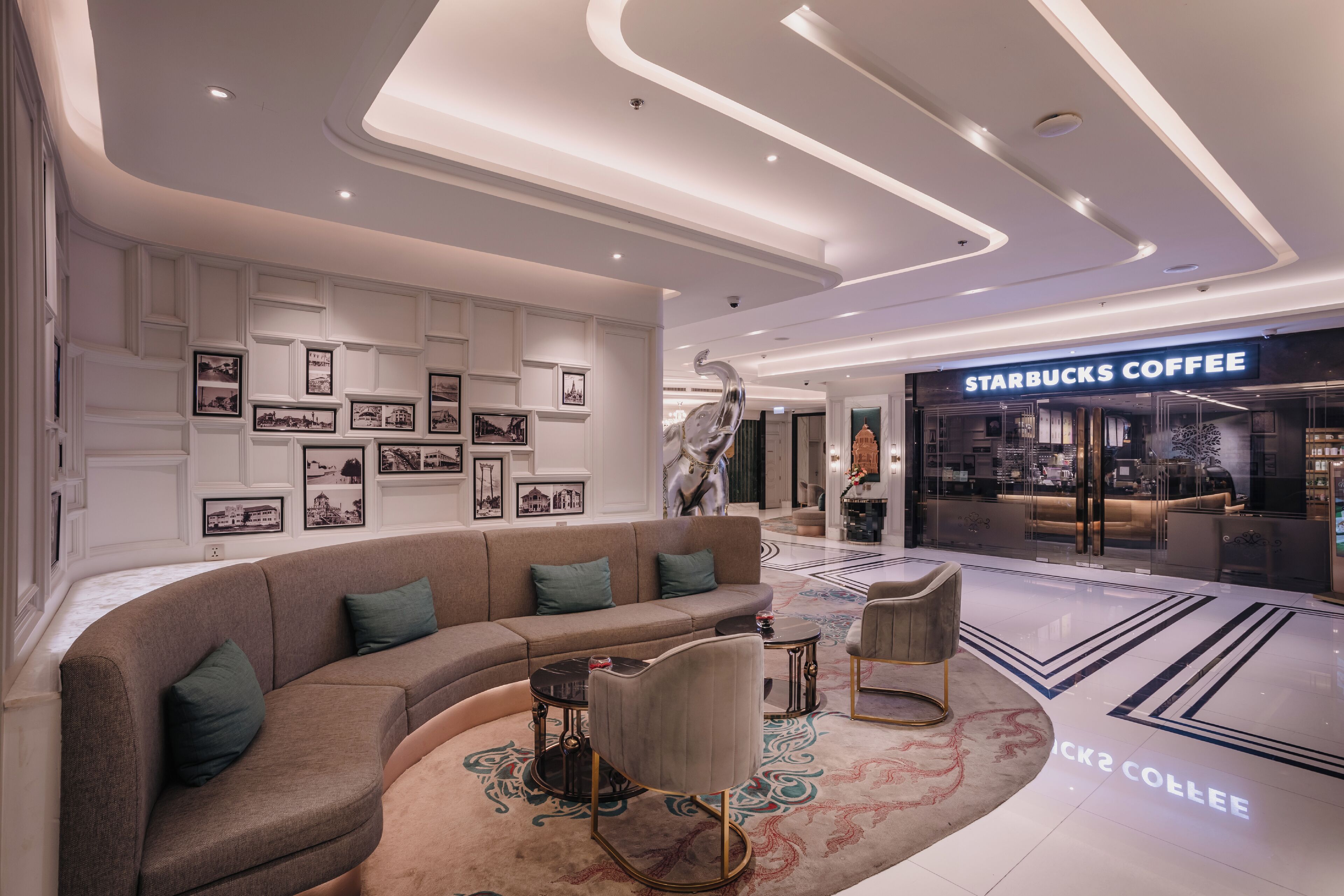 A modern lobby with a curved sofa, a coffee shop, and framed pictures on the wall.