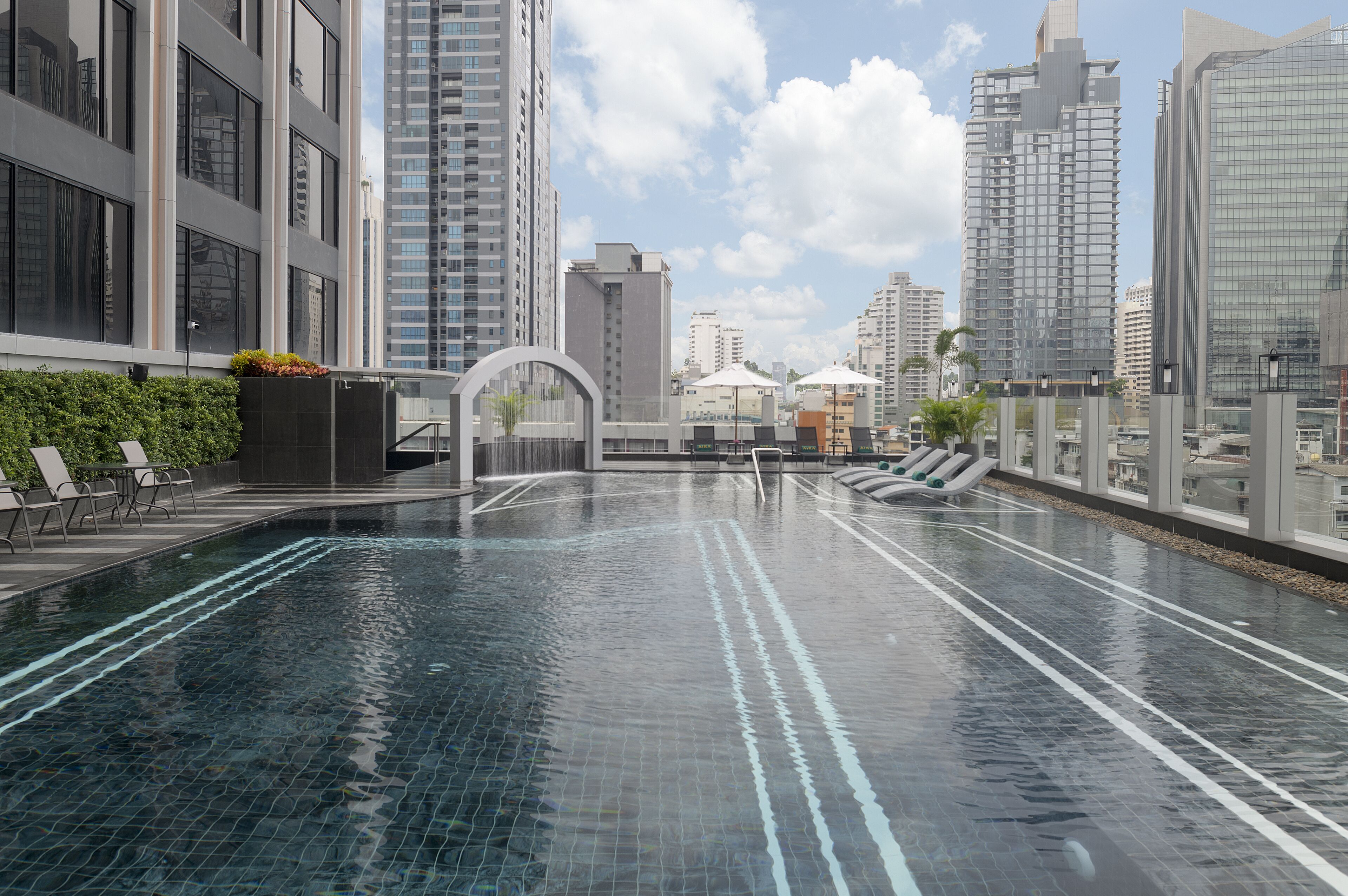 A rooftop swimming pool with clear water, surrounded by high-rise buildings and a clear sky.