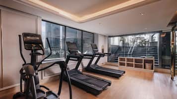 A modern gym with treadmills, an elliptical, and a stair climber, large windows, and a view of the city.
