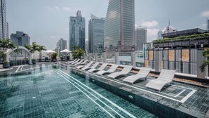 Ein Rooftop-Infinity-Pool mit Liegestühlen, umgeben von Hochhäusern und Palmen.