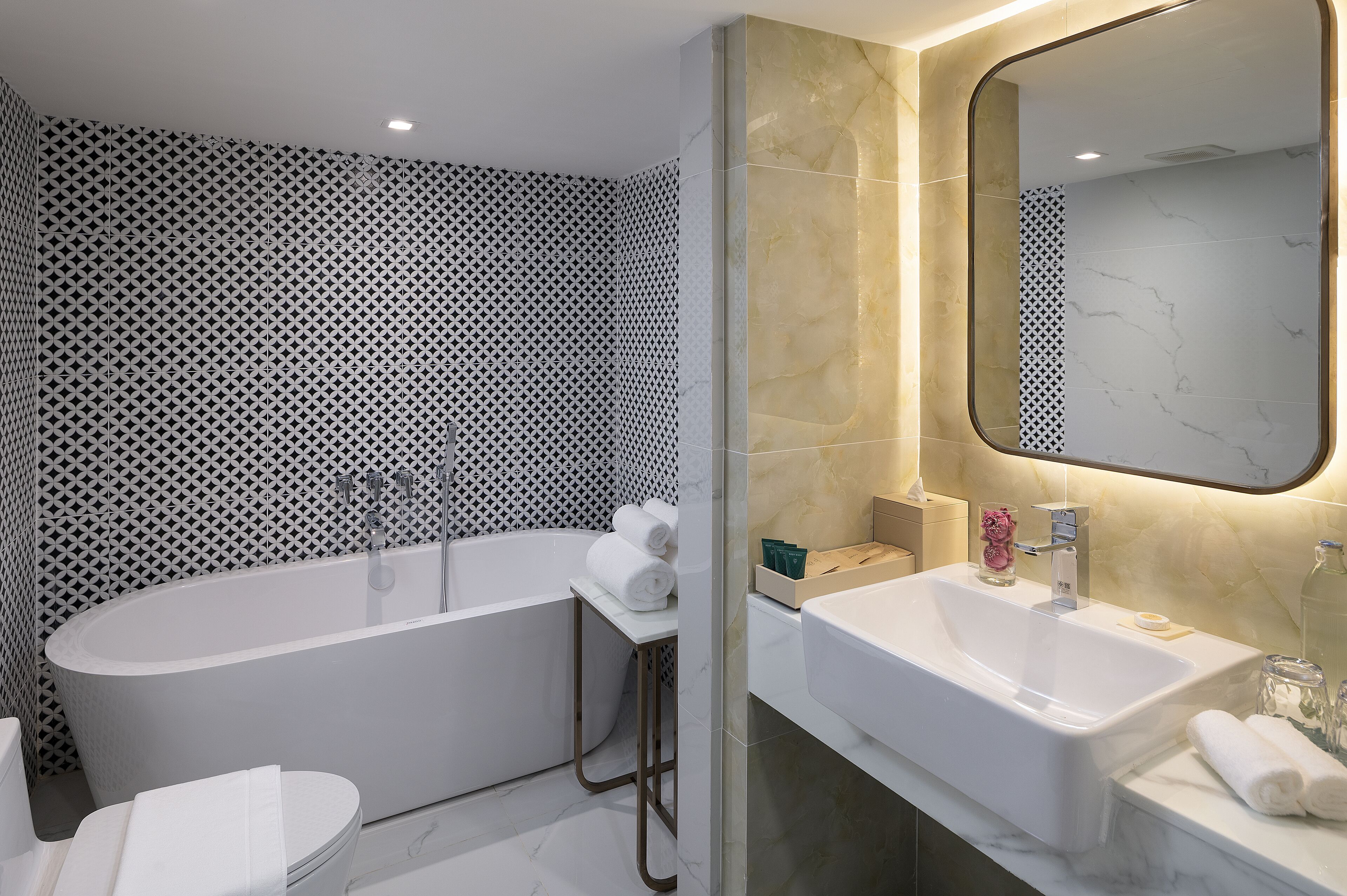 A modern bathroom with a freestanding bathtub, a vanity with a mirror, and patterned walls.