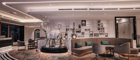 A modern lobby with a central seating area featuring a large elephant sculpture, a patterned carpet, and a wall adorned with framed pictures.