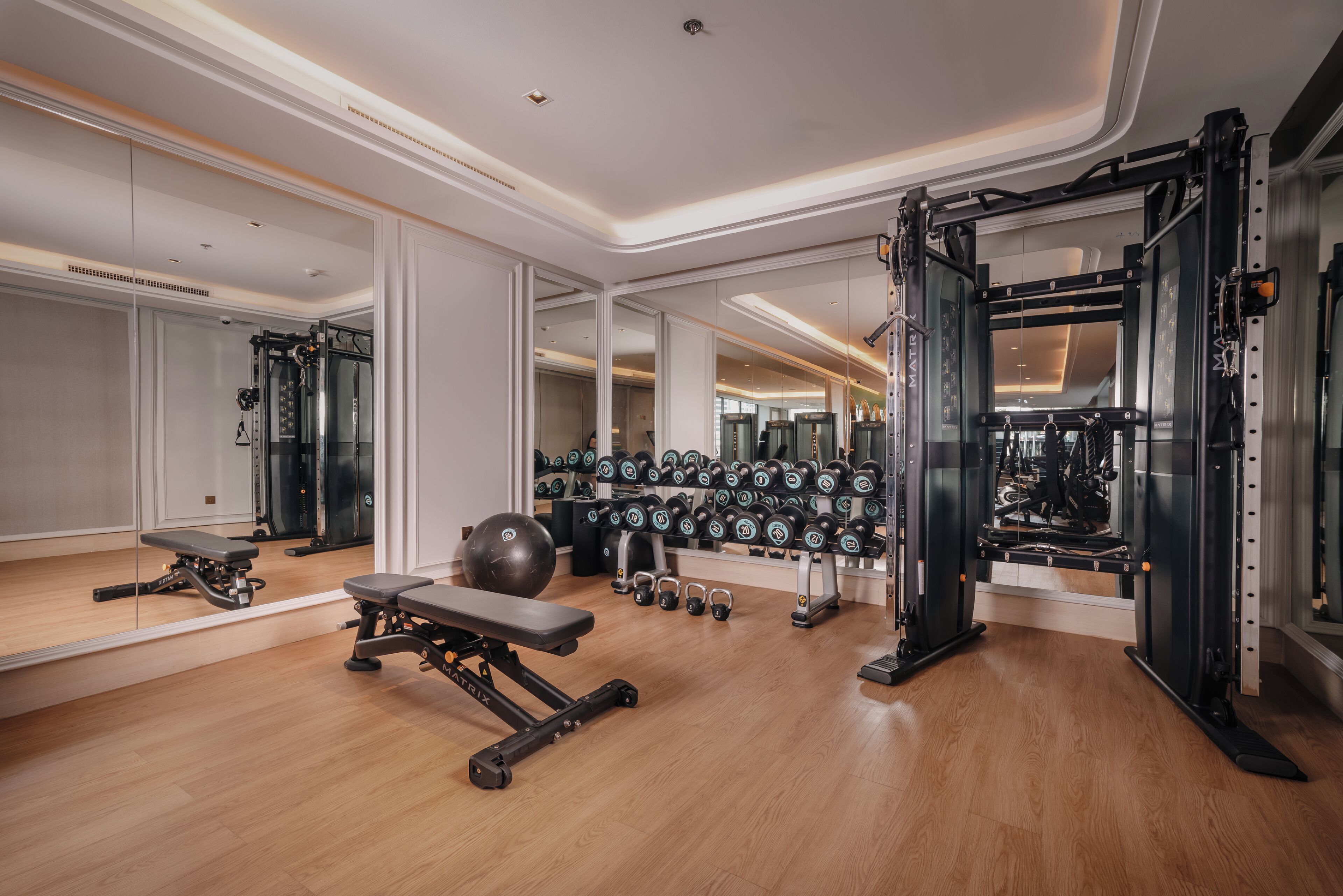 A modern gym with mirrored walls, various exercise equipment, and a wooden floor.