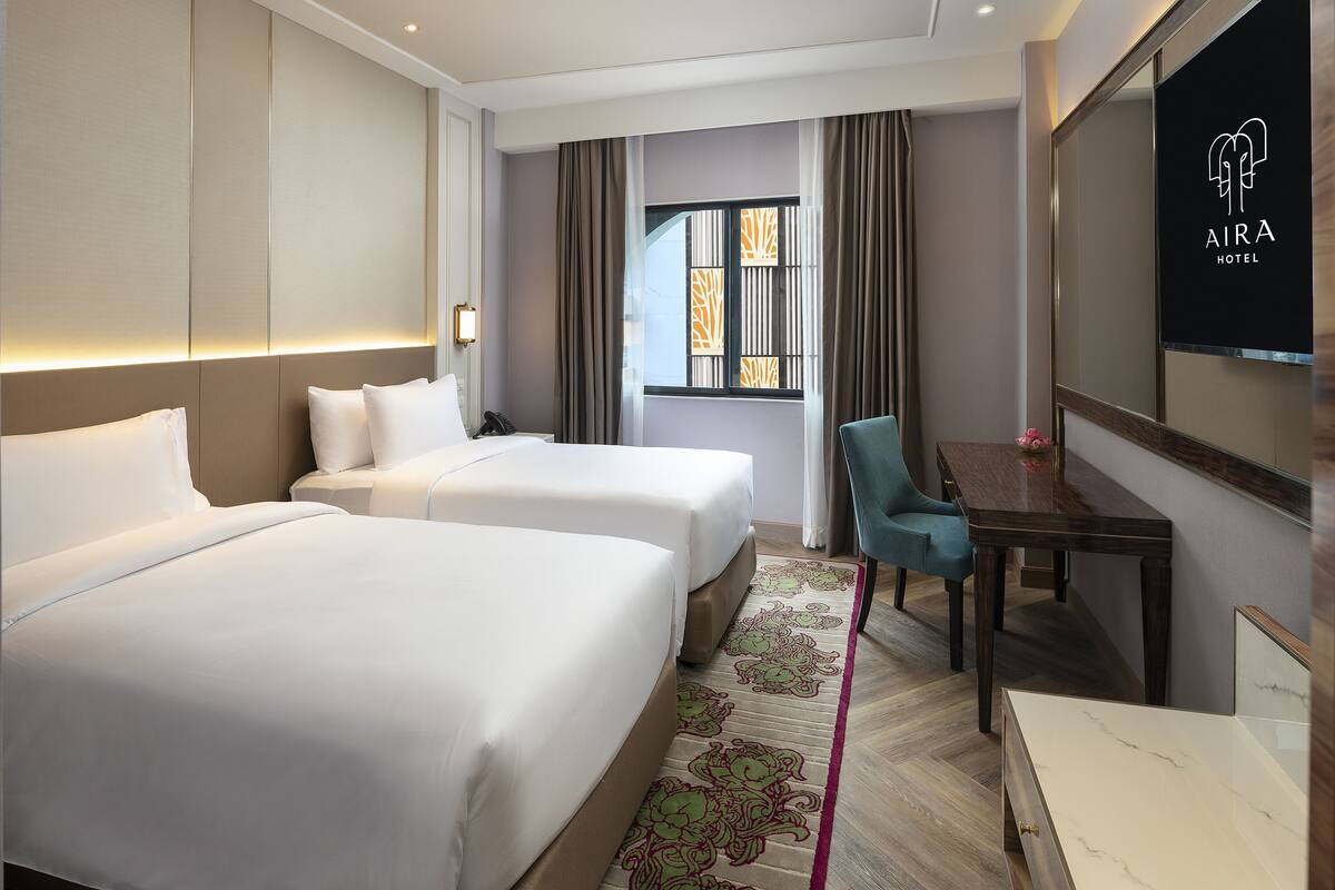 Habitación de hotel con dos camas, un escritorio, una silla, un espejo grande y una ventana con cortinas.