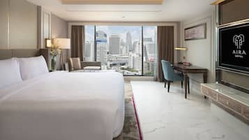 A hotel room with a large bed, a desk, a chair, a TV, and a city view.
