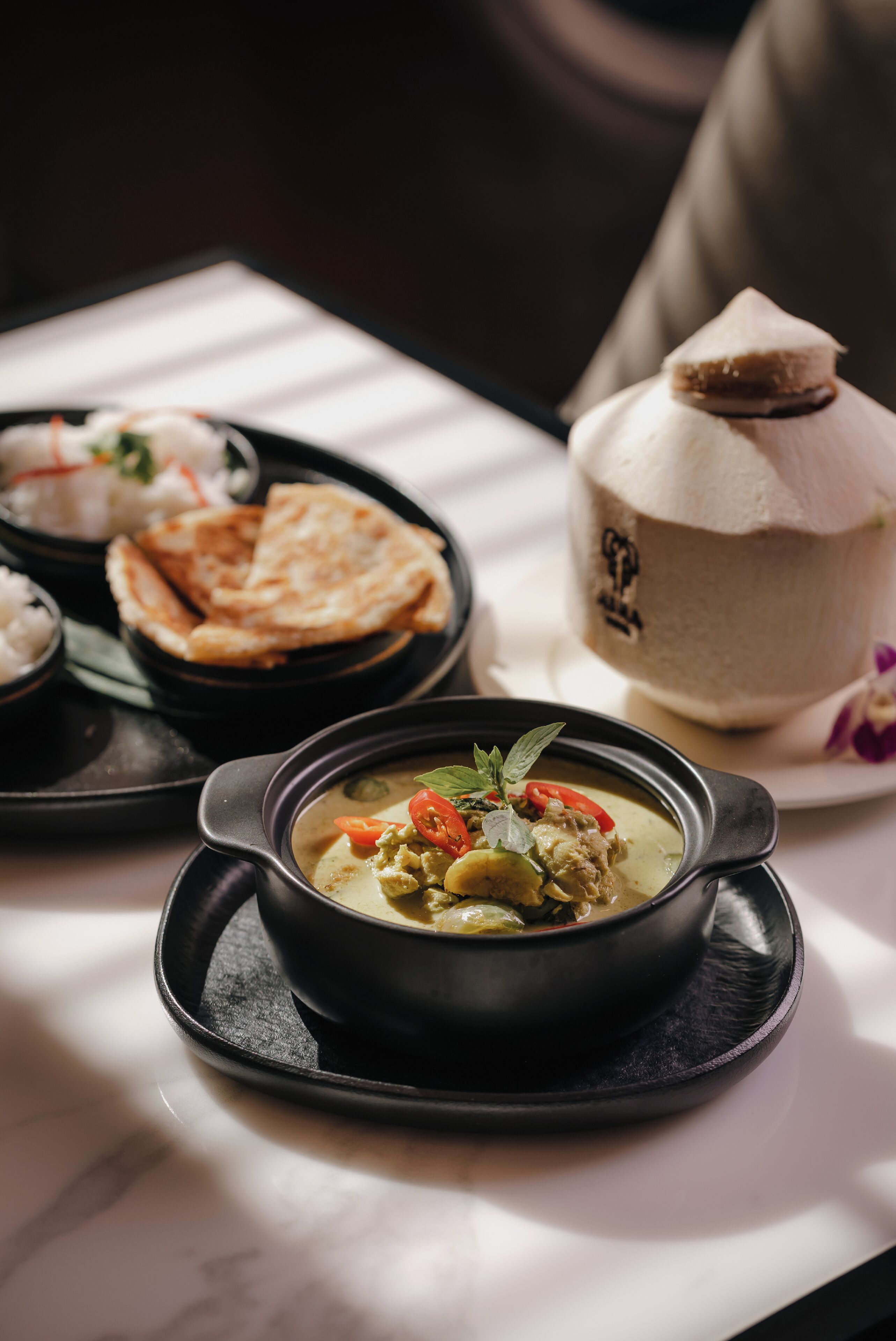 A table with a bowl of soup, flatbread, and a covered container, likely a dessert or beverage.