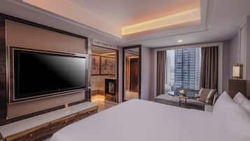 A modern hotel room with a large bed, a flat-screen TV, a fireplace, a seating area with a table, and a view of the cityscape.