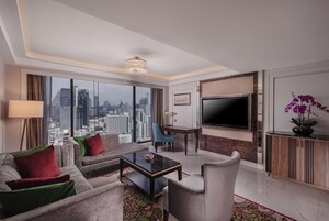 A modern hotel room with a city view, a flat-screen TV, a dining area, and a seating area with a coffee table.